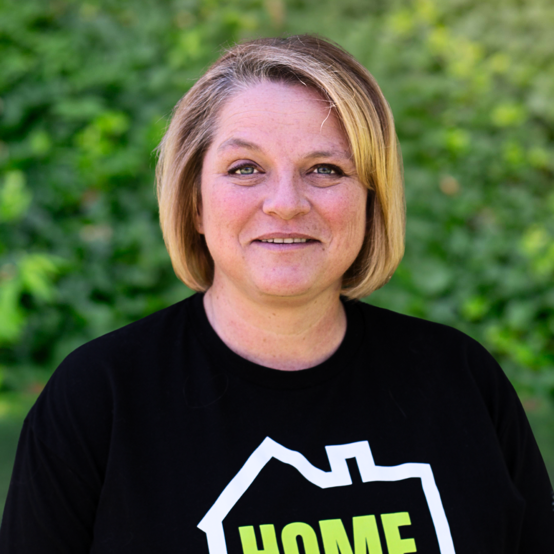 Woman with blonde bob smiles, wearing a black shirt against a gray background.