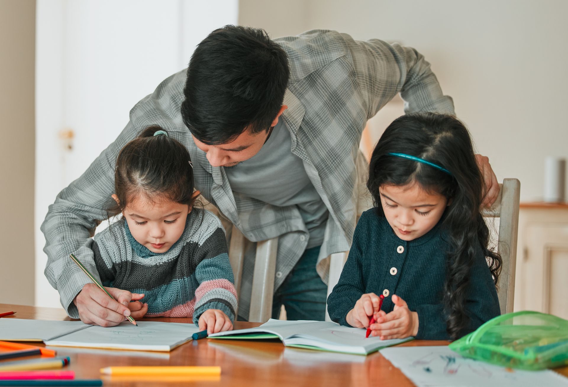Man helps two children with homework at a table.