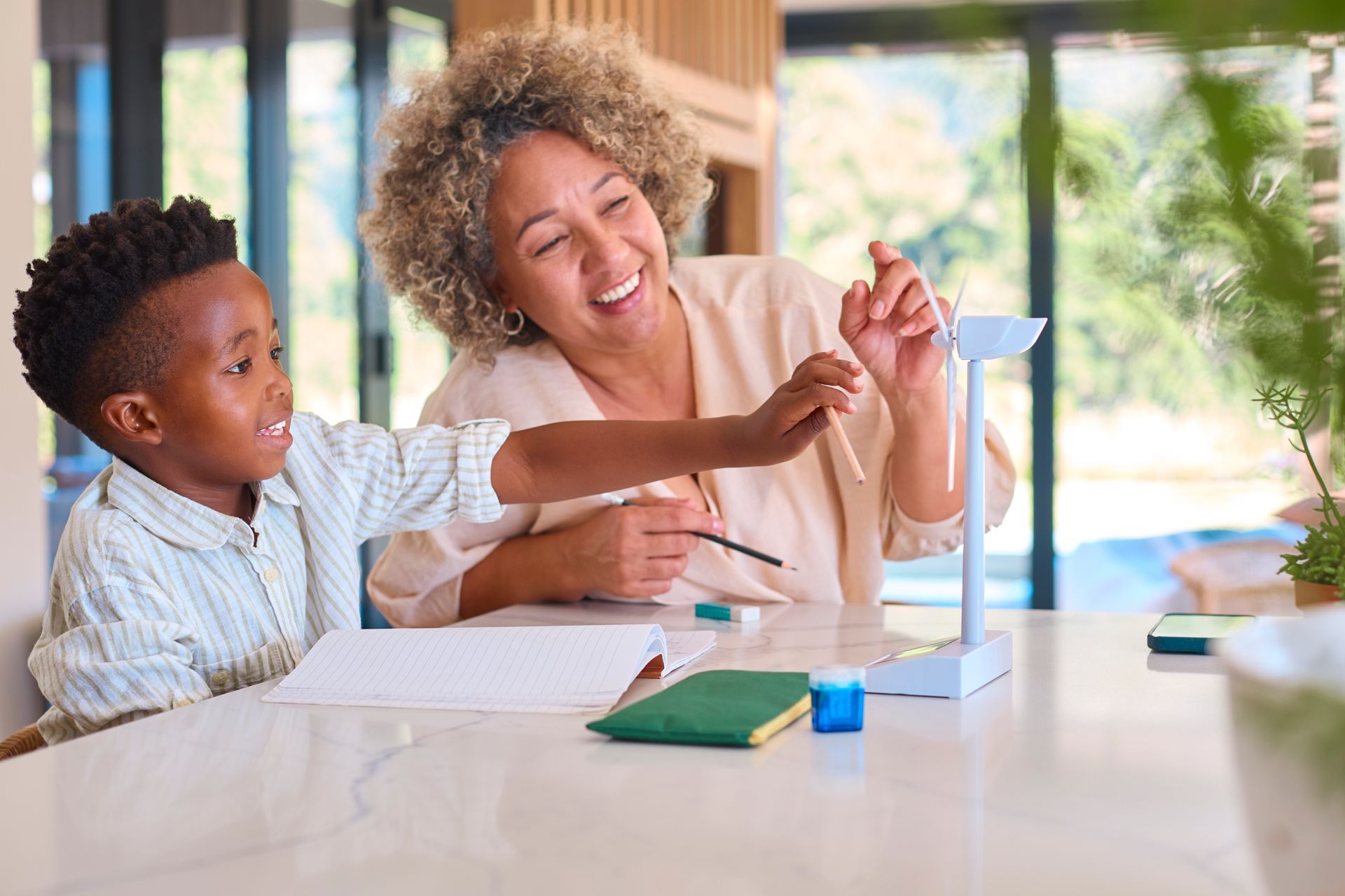 Woman and child painting a model windmill at a table. Both smile, appear happy. Bright, indoor setting.