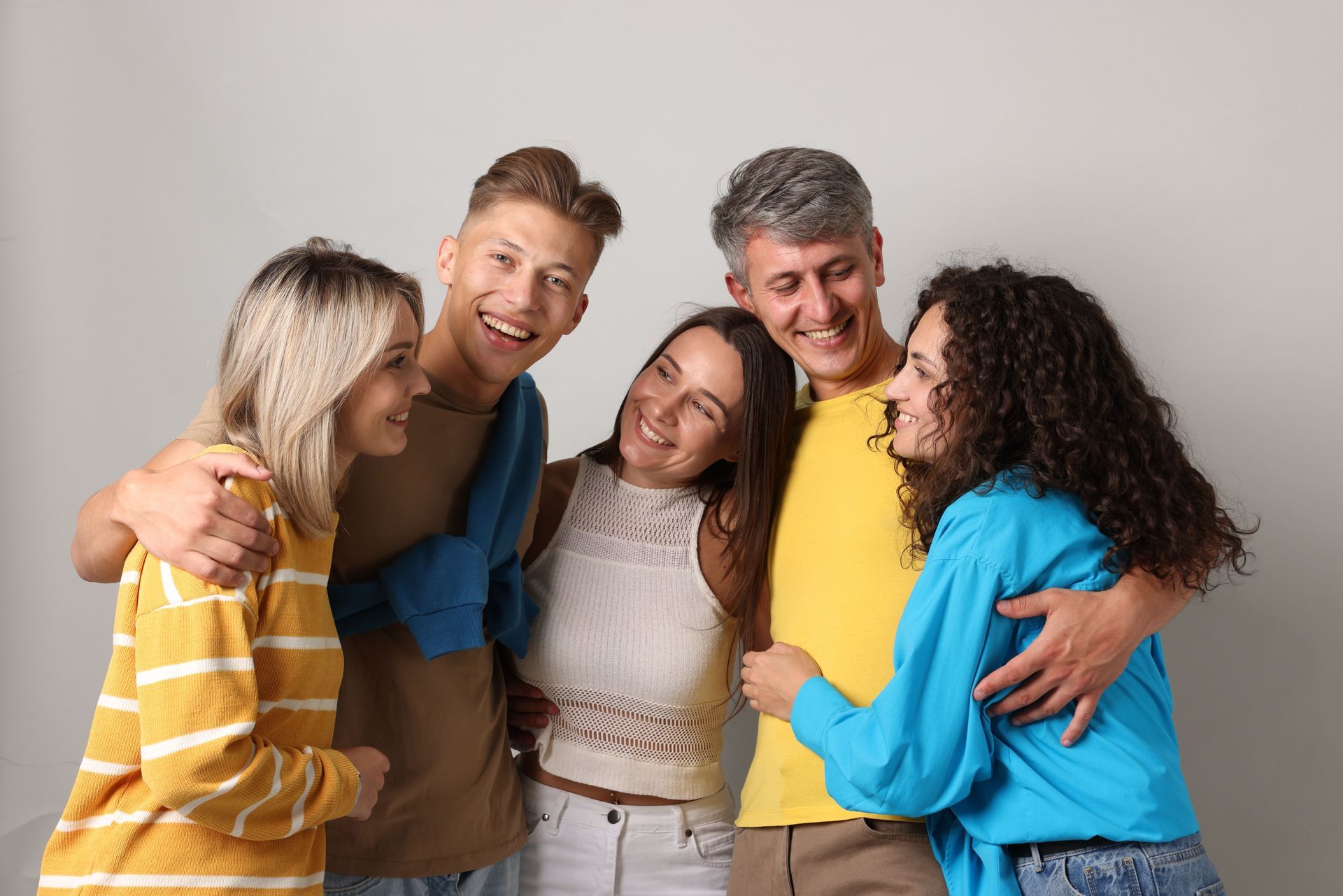 Five people, arms around each other, smiling and laughing in front of a gray backdrop.