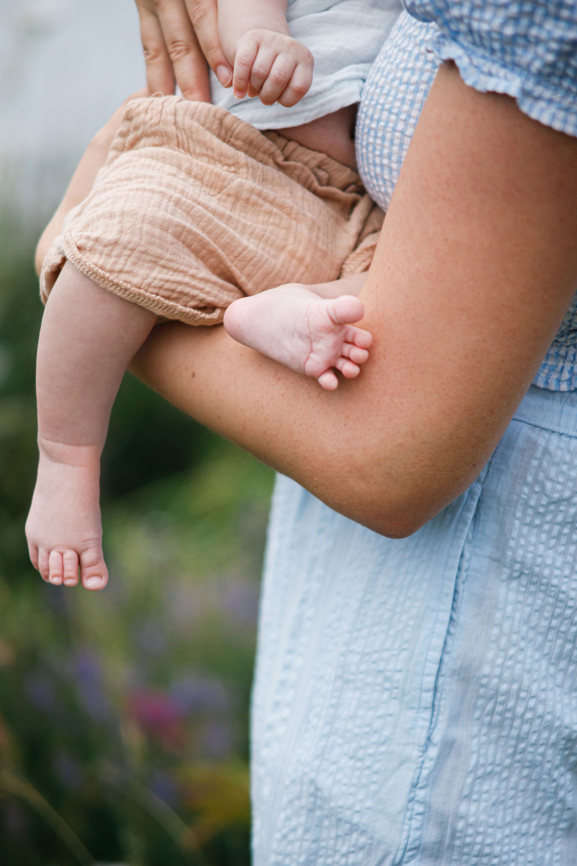 Parents with baby on a blanket in the grass. Woman looks down, man touches baby's head.