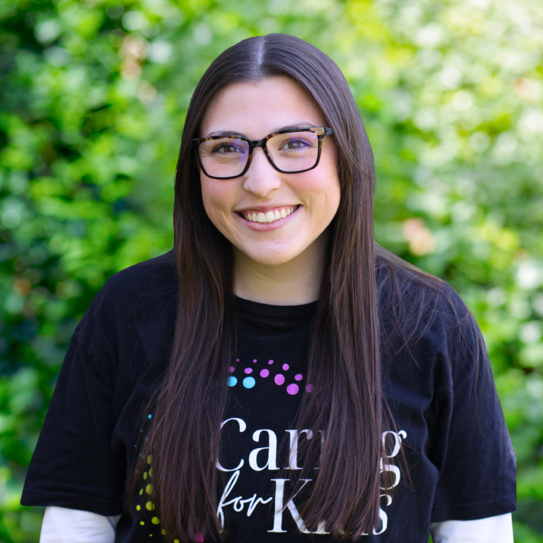 Woman with glasses, smiling, wearing a green shirt, against a white backdrop.