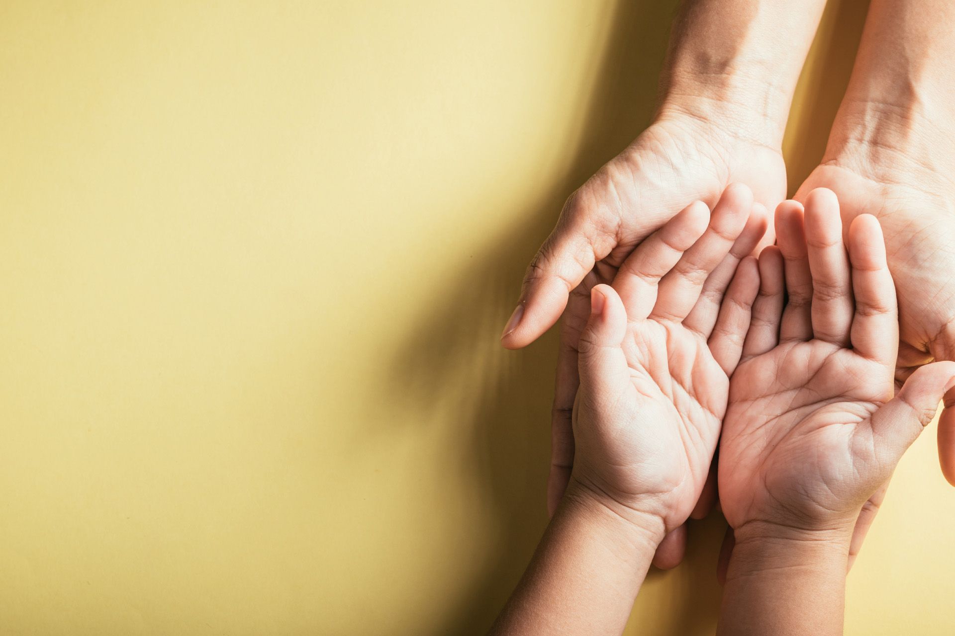Adult hand cradling a child's hand, both open, on a yellow background.