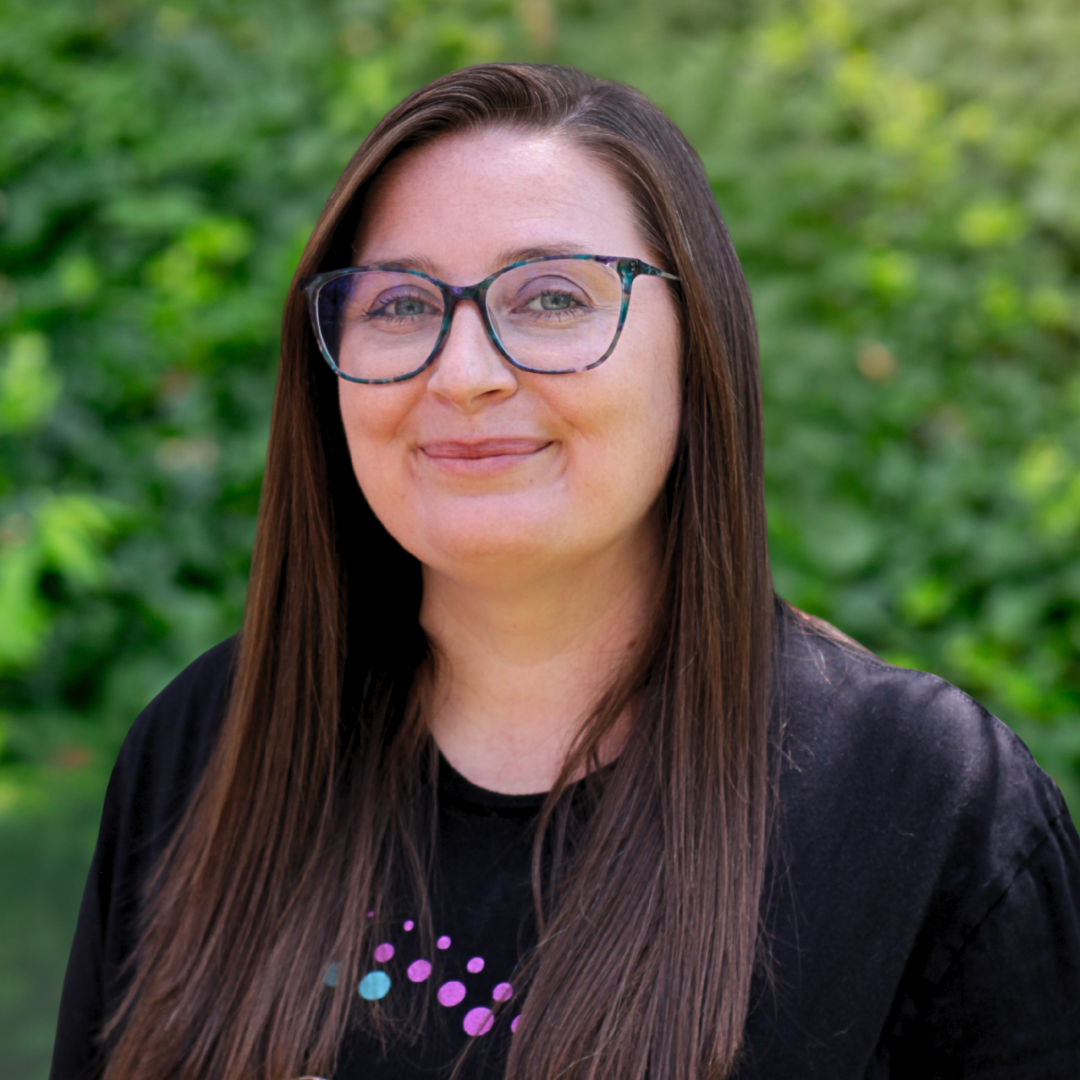 Woman with glasses and brown hair, smiling, wearing a black cardigan over a green shirt.