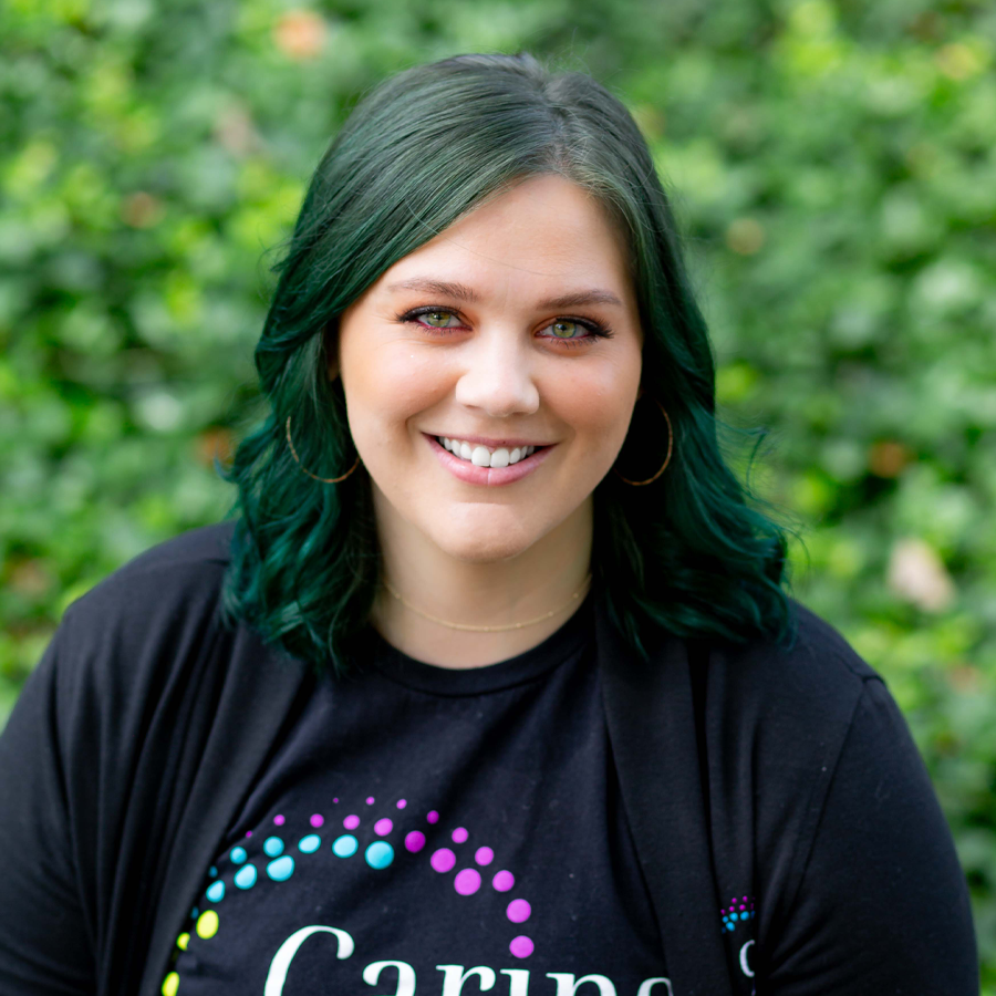 Woman with green hair smiles wearing a black t-shirt outdoors.