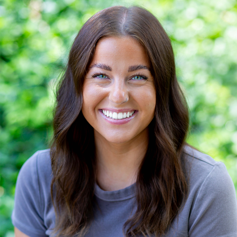 Woman with shoulder-length brown hair smiles, wearing a patterned sweater and gold necklace.