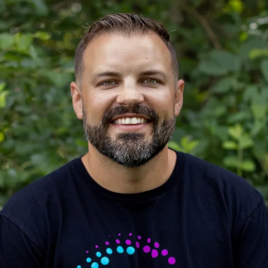 Man in blue shirt smiles at the camera; neutral background.