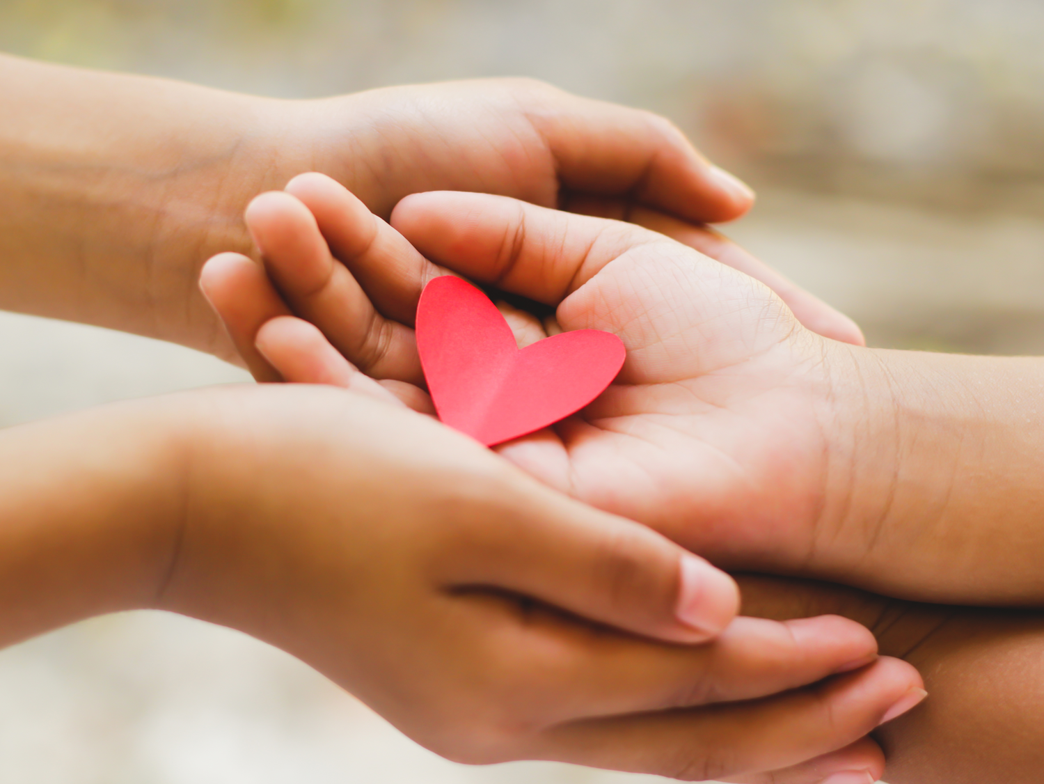 Two pairs of hands holding a small red paper heart.