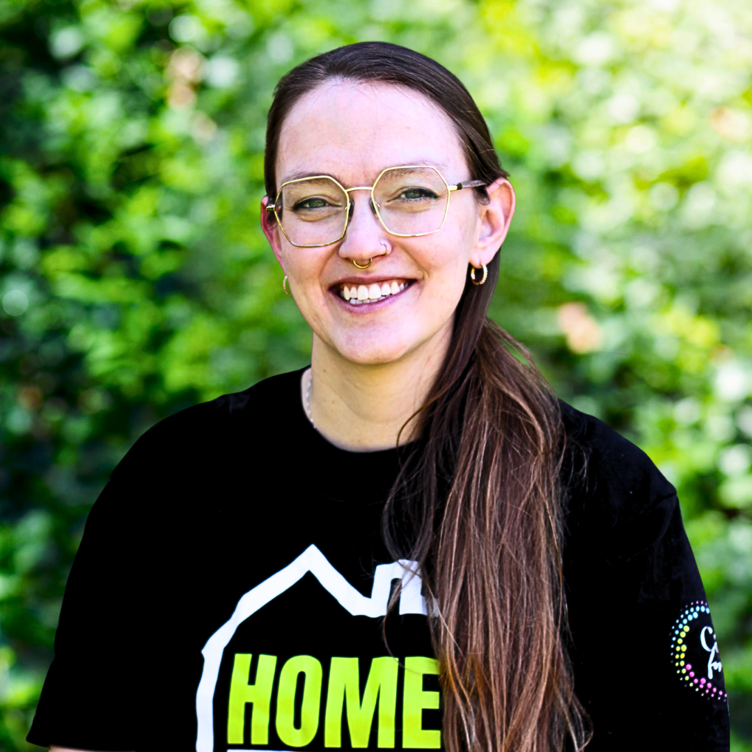 Woman with glasses and nose ring smiles, wearing a black shirt.