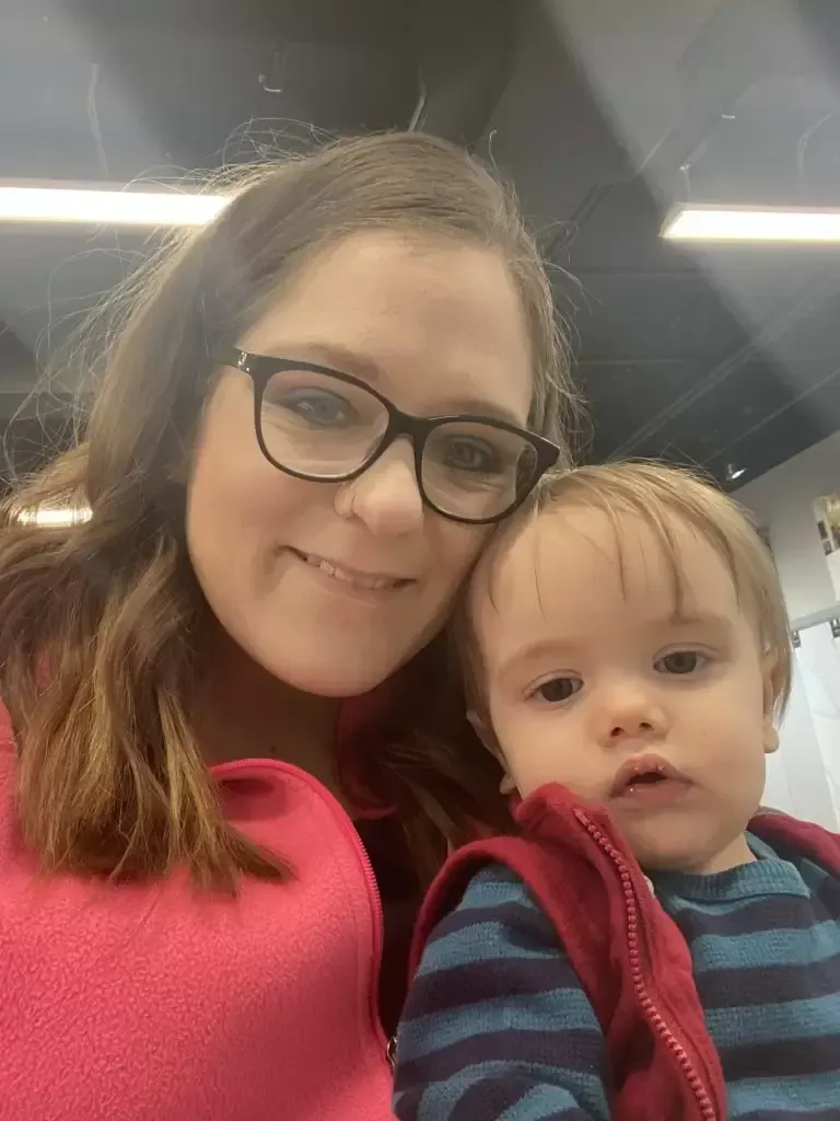 Woman with glasses and a young child, smiling at the camera. They are indoors, close together.