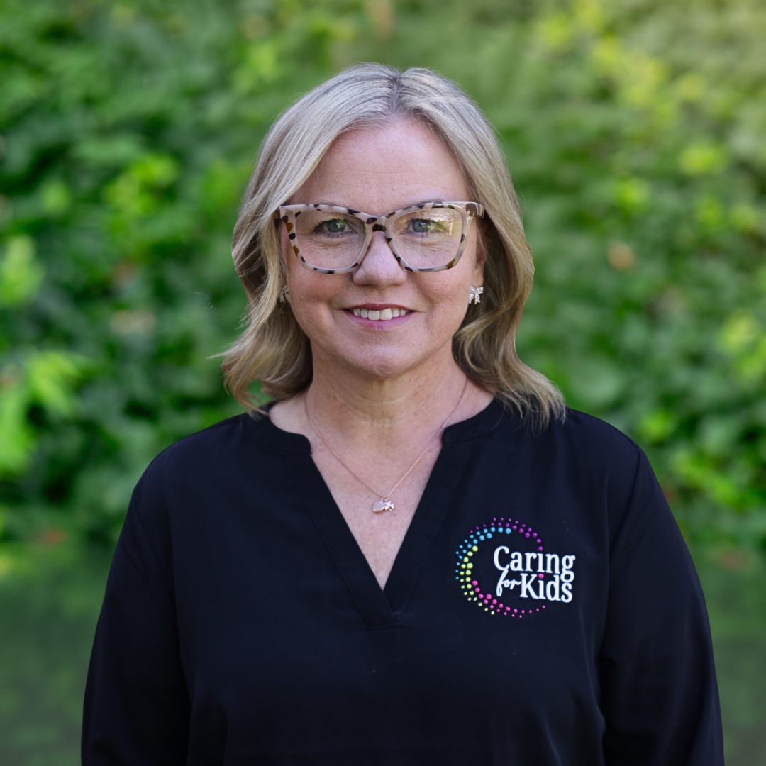 Blonde woman wearing glasses, black sweater, and plaid earrings smiles at the camera.