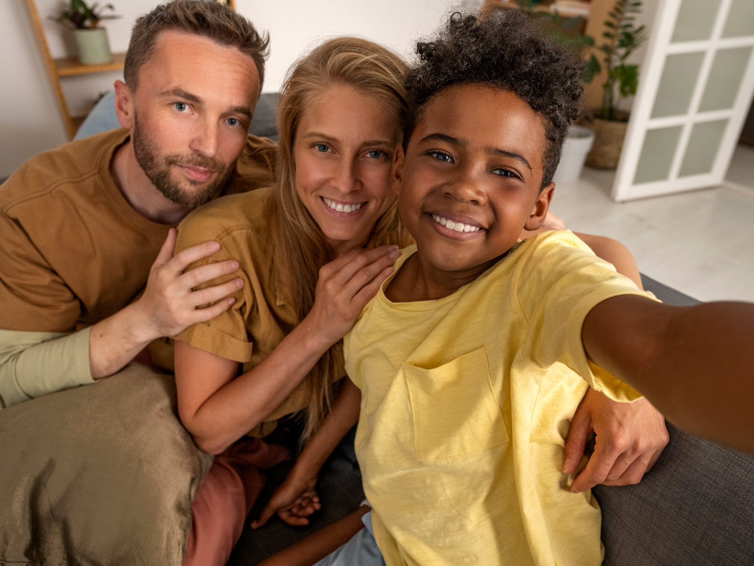 Family of three smiling, taking a selfie on a couch.