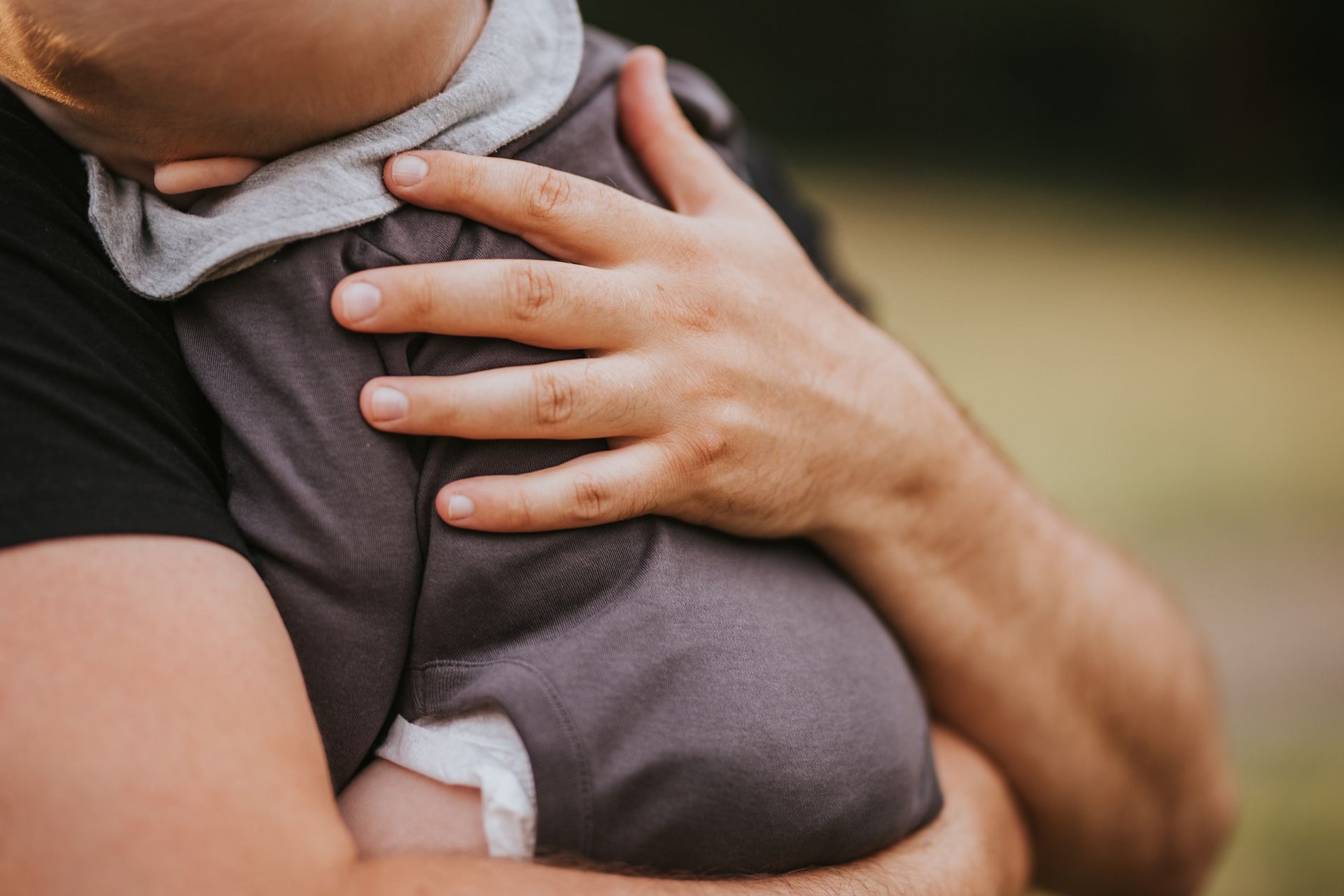 Parents with baby on a blanket in the grass. Woman looks down, man touches baby's head.