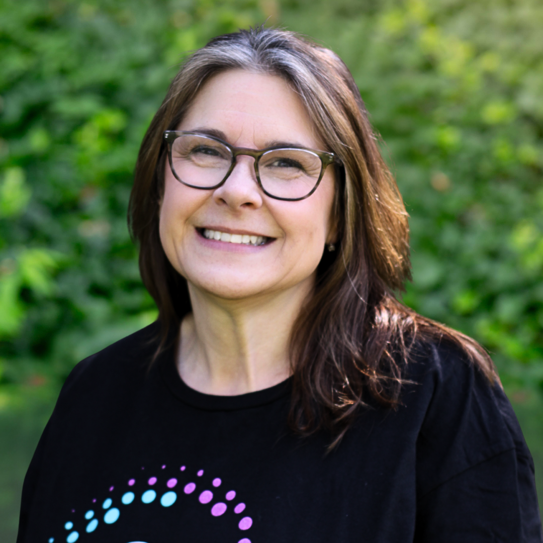 Woman wearing glasses and a purple cardigan smiling at the camera.