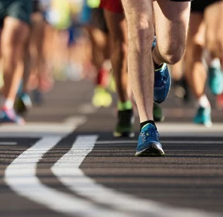 Runners' legs and feet in motion on a paved road, with white lane markings.
