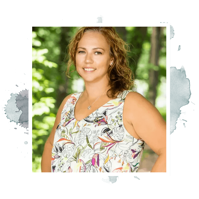 Woman with curly hair smiles, wearing a floral tank top outdoors with trees in the background.