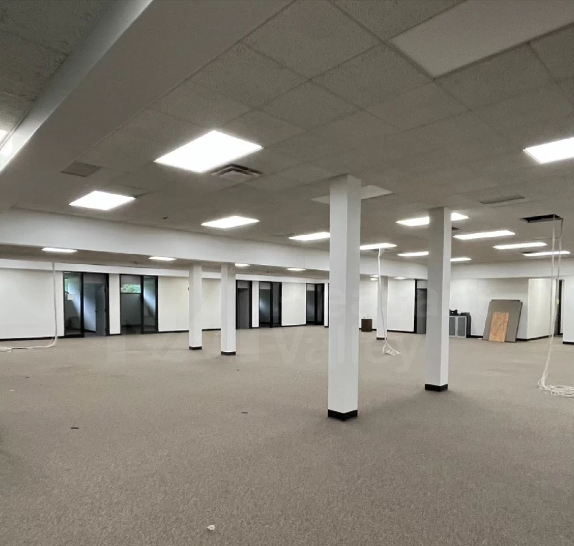 Large, empty commercial space with white columns, carpet, and glass doors.