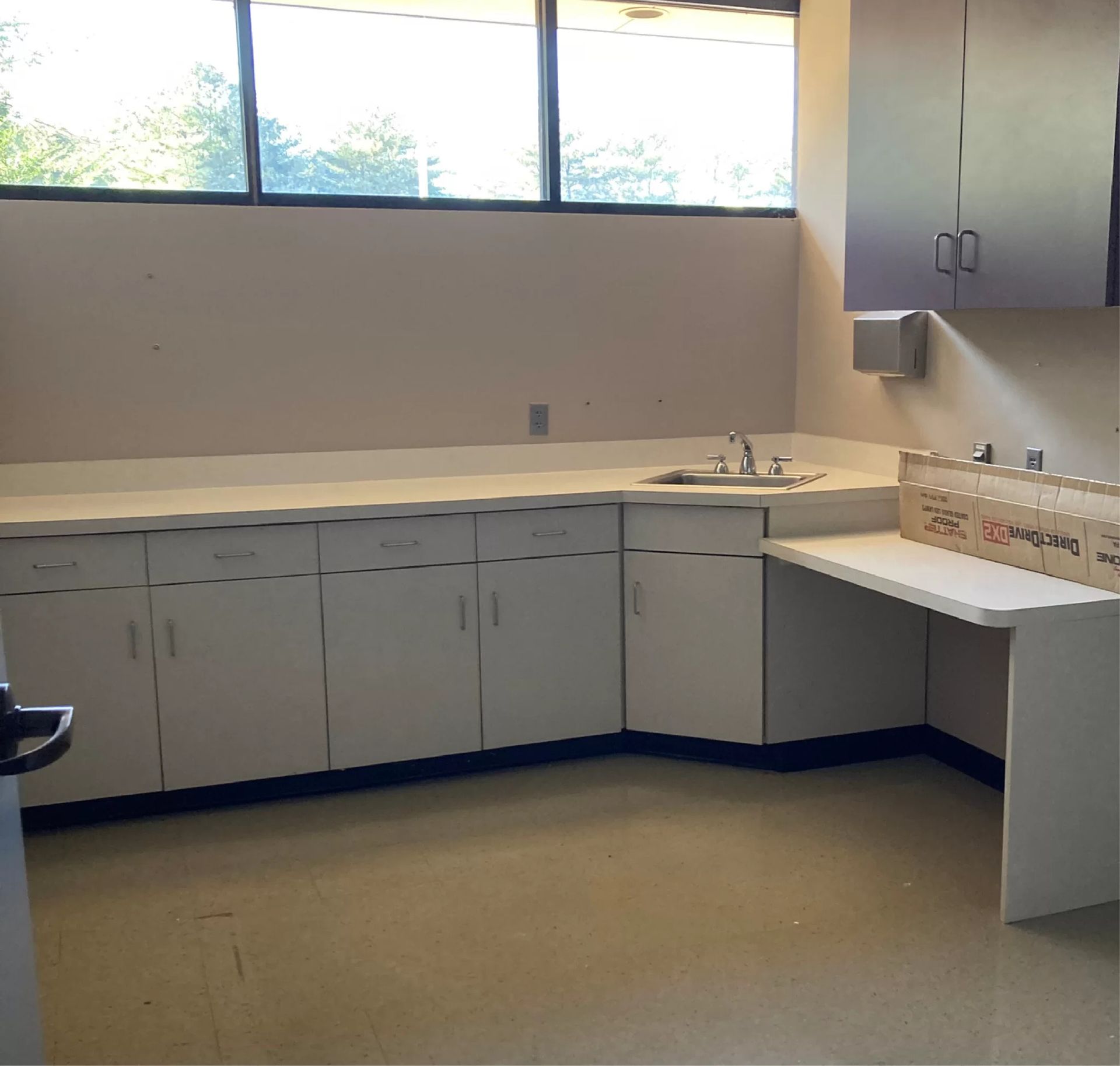 Empty room with white cabinets, sink, and window.