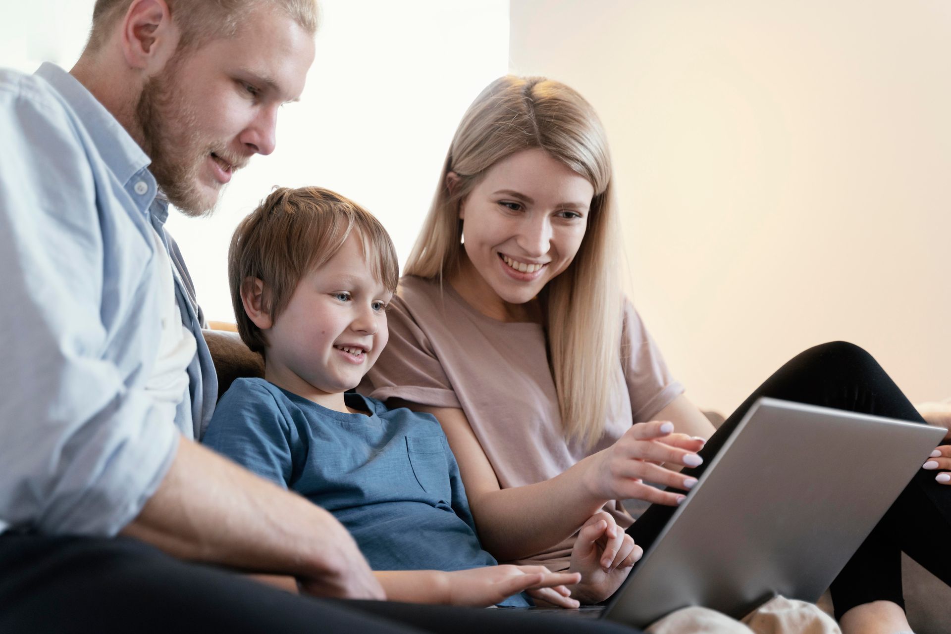 A family of three smiling, looking at a laptop together, sitting on a couch.