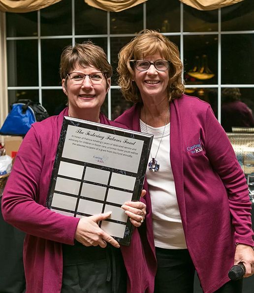 Two women in magenta jackets smiling, holding an award plaque.