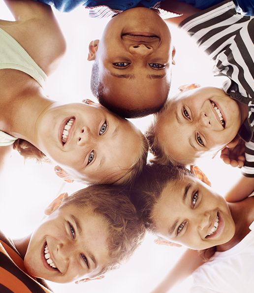 Smiling children of diverse ethnicities huddle together, looking down.
