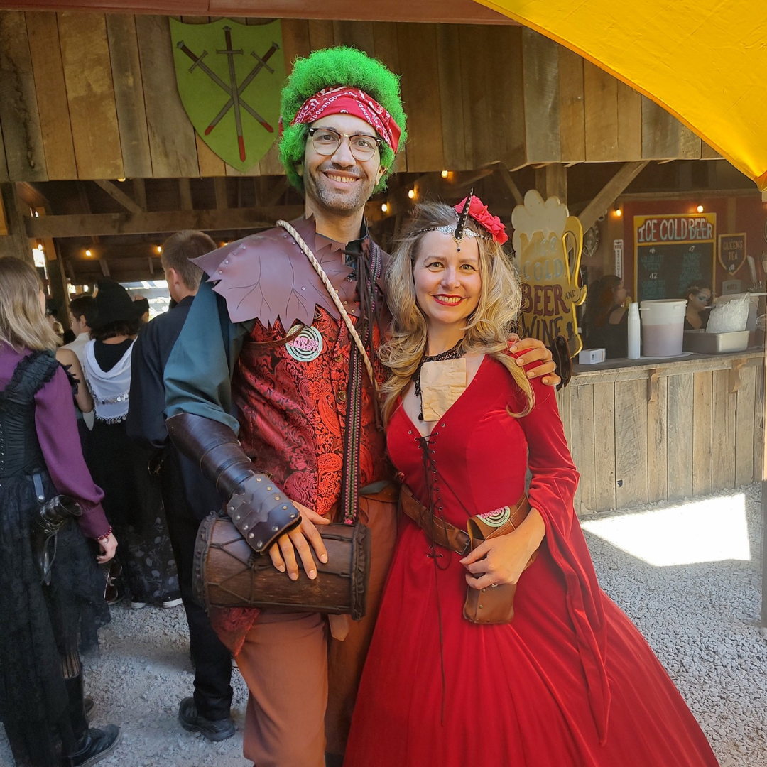 Man and woman in Renaissance fair costumes; man with green hair, woman in red dress.