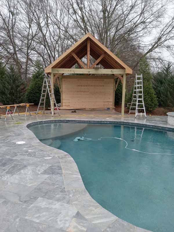A wooden structure, under construction, next to a pool. Two ladders lean against it.