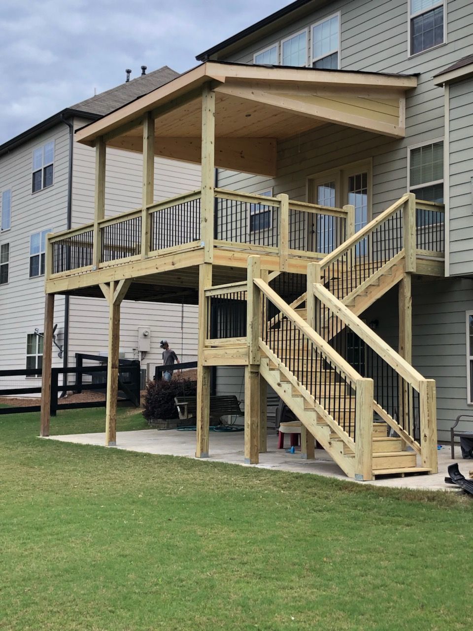 Wooden deck with stairs, black railings, and covered portion extending from a two-story house.
