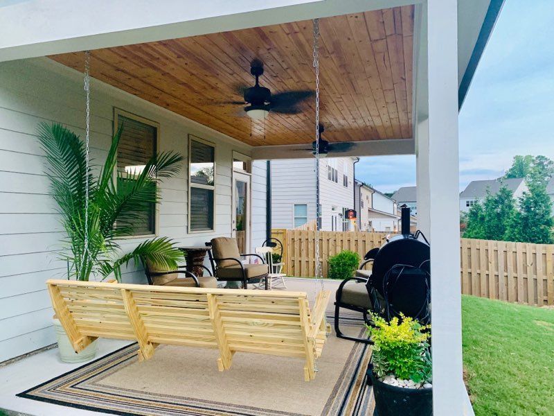 Covered patio with a wooden swing, seating, and a ceiling fan.
