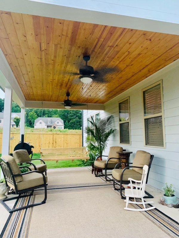Covered patio with wood ceiling, ceiling fans, seating, and view of a yard.