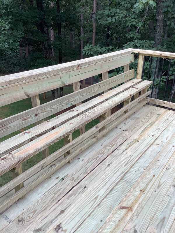 Wooden deck with built-in bench and backrest; surrounded by trees.