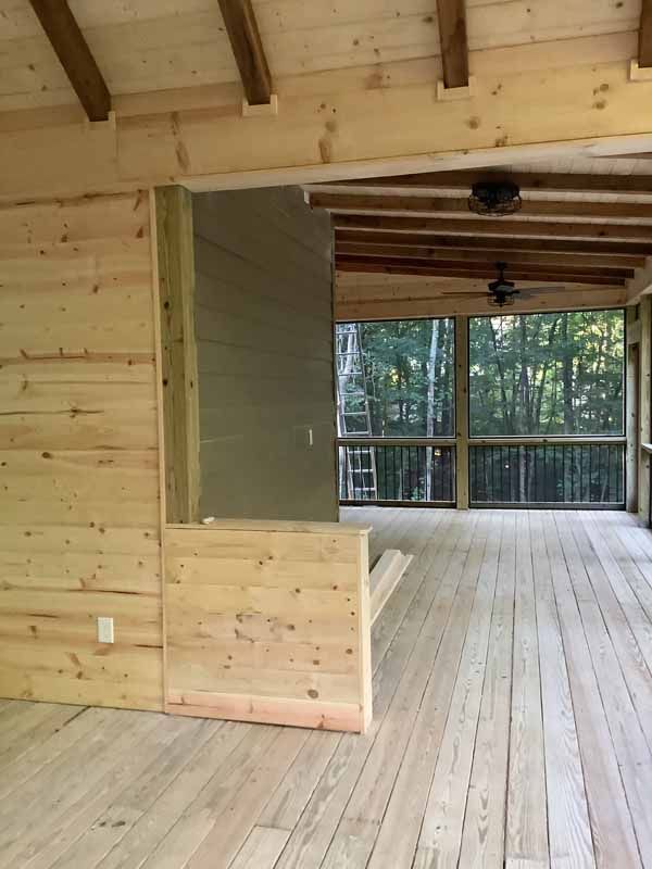 Wooden porch under construction; interior walls with exposed wood and steps leading to screened porch.