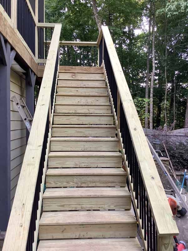 Wooden outdoor staircase leading up to a deck, black railing, light wood steps.