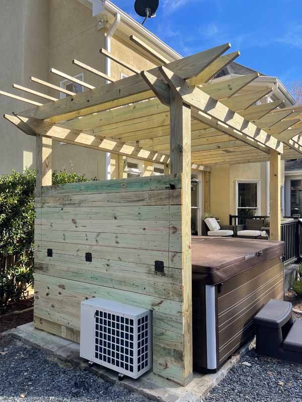 Wooden pergola over a hot tub, next to a building. Air conditioning unit visible.