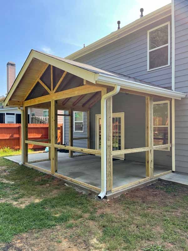 A screened-in porch addition with a gabled roof attached to a gray house.