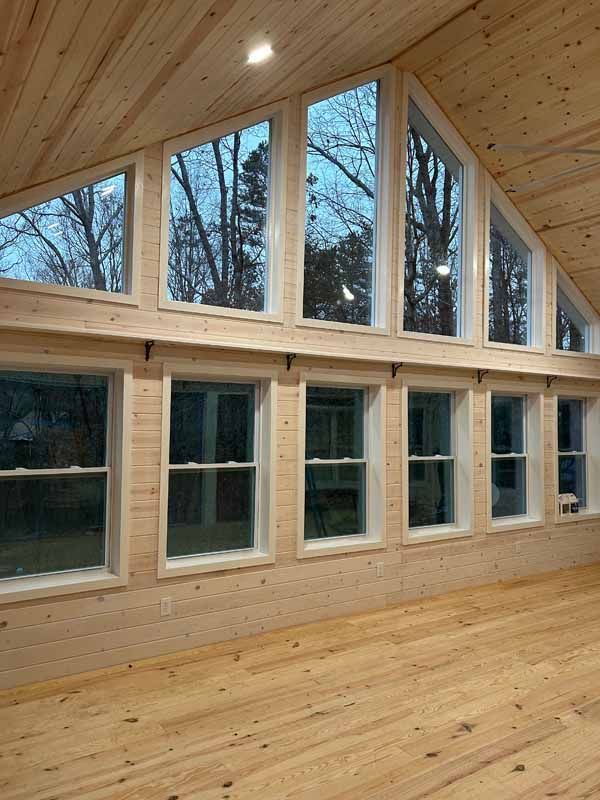 Interior view of a light-filled room with wood paneling and multiple windows offering a view of bare trees.