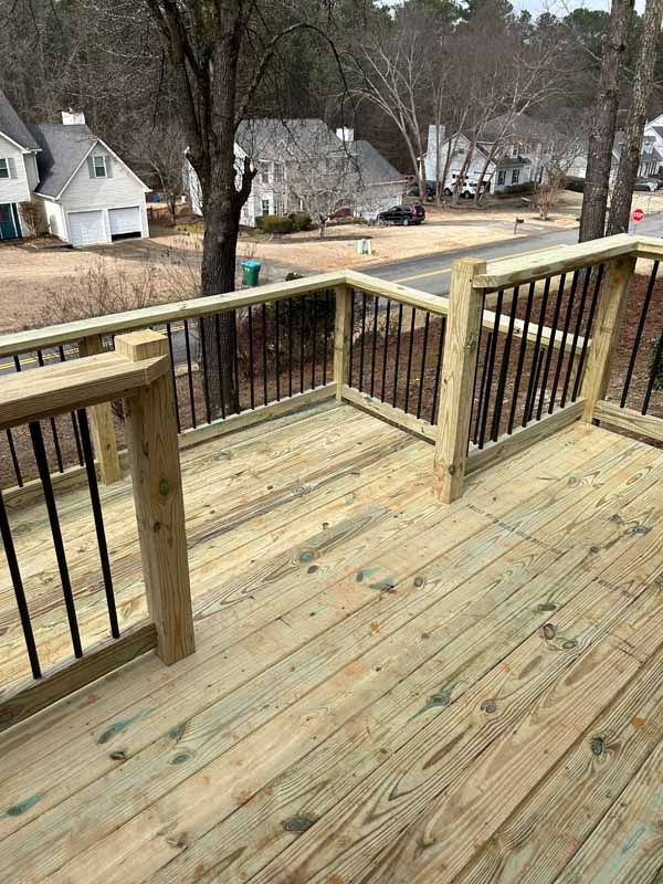 Wooden deck with black metal railing overlooking a residential street and houses on a clear day.