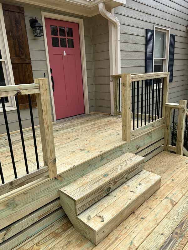 Wooden front porch with stairs and black railings leading to a pink door.
