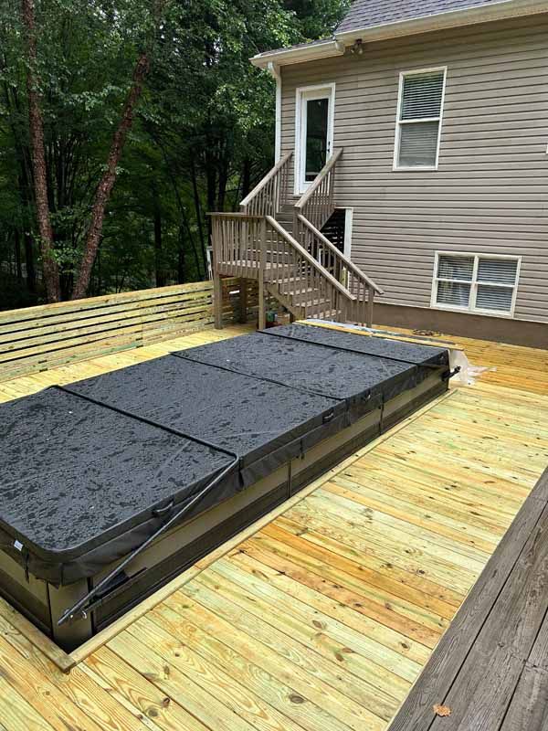 A covered rectangular hot tub on a wooden deck next to a house with stairs.