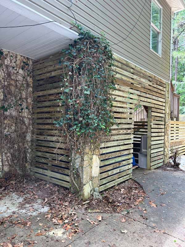 Exterior of a building with wooden slat walls, a stone pillar, and climbing greenery.