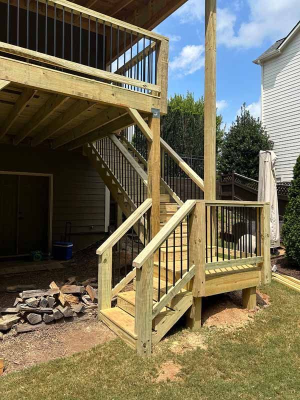 Multi-level wooden deck with stairs and black metal railings in a backyard.