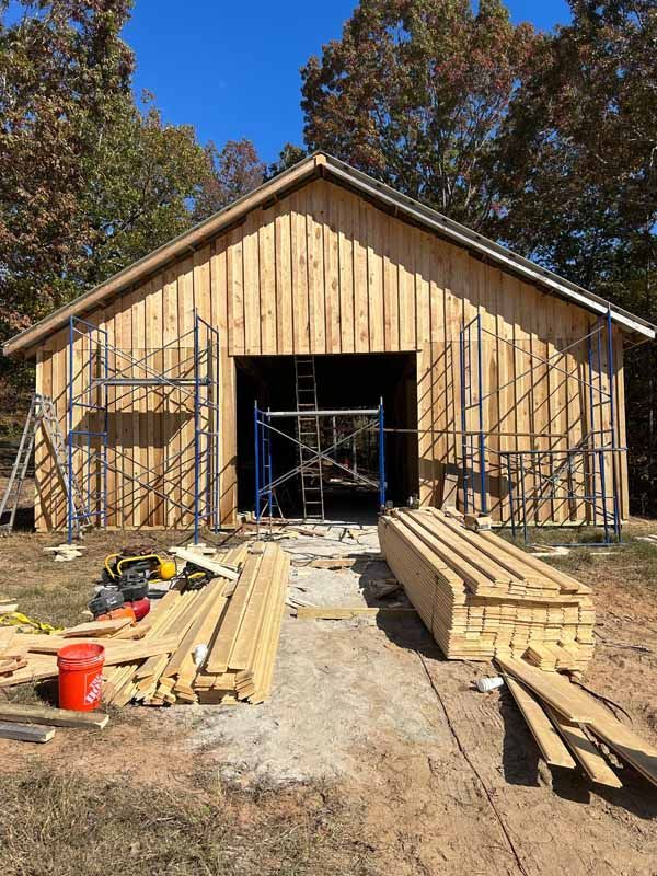 Wooden barn under construction with scaffolding and lumber on the ground.