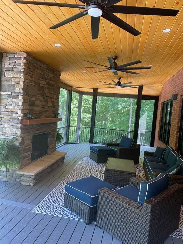 Screened-in porch with fireplace, seating area, and ceiling fans. Stone fireplace and wood ceiling.