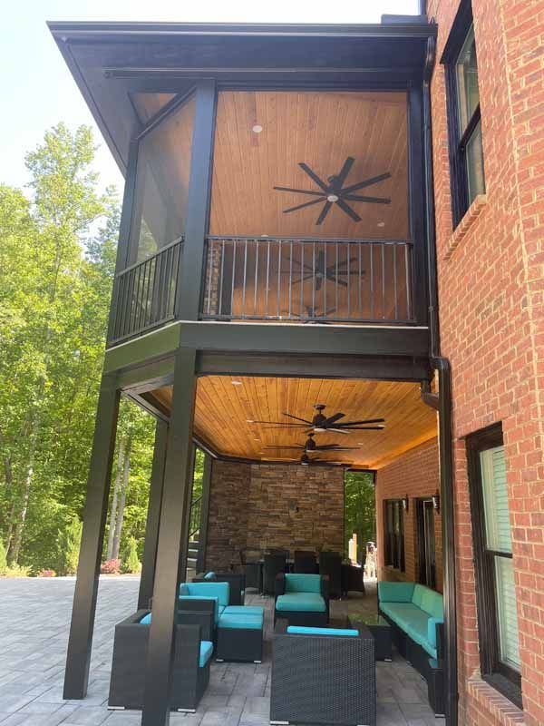 Two-story screened porch with black frame, wood ceiling, ceiling fans, and outdoor furniture.
