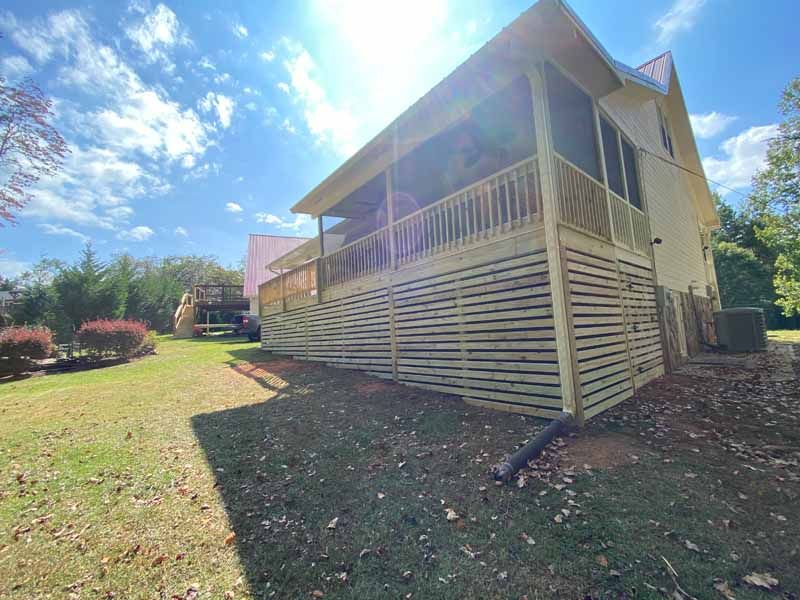 Wooden deck and screened porch attached to a light-colored house under a partly cloudy sky.