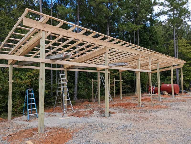 Wooden carport frame under construction outdoors, with ladders and a propane tank.