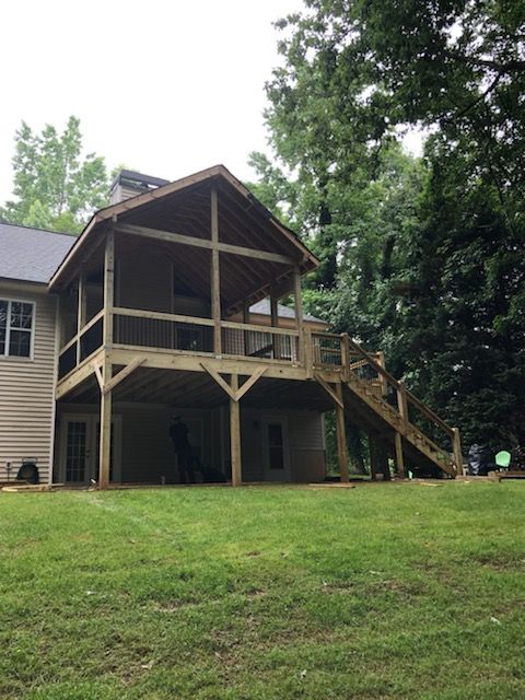 Wooden screened porch and deck on the back of a house with stairs, grassy yard, and trees.