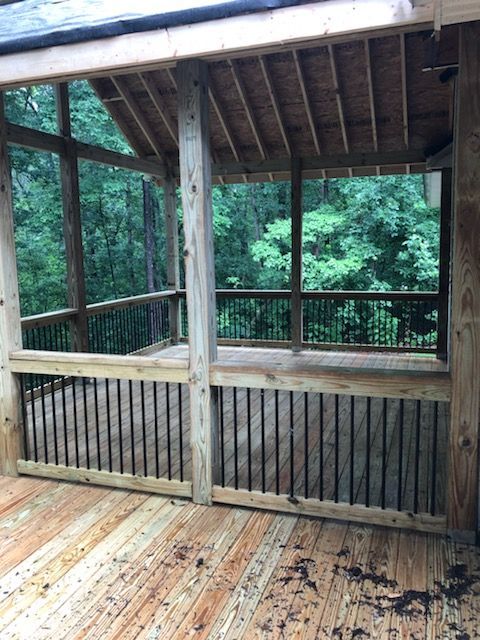 Wooden screened porch overlooking a wooded area. The porch has a wooden floor, railing, and ceiling.