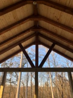 Wooden ceiling and beams, with a view of trees and sky through a triangular frame.