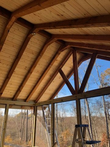 Wooden roof of a screened porch, with glass windows, overlooking a wooded landscape.